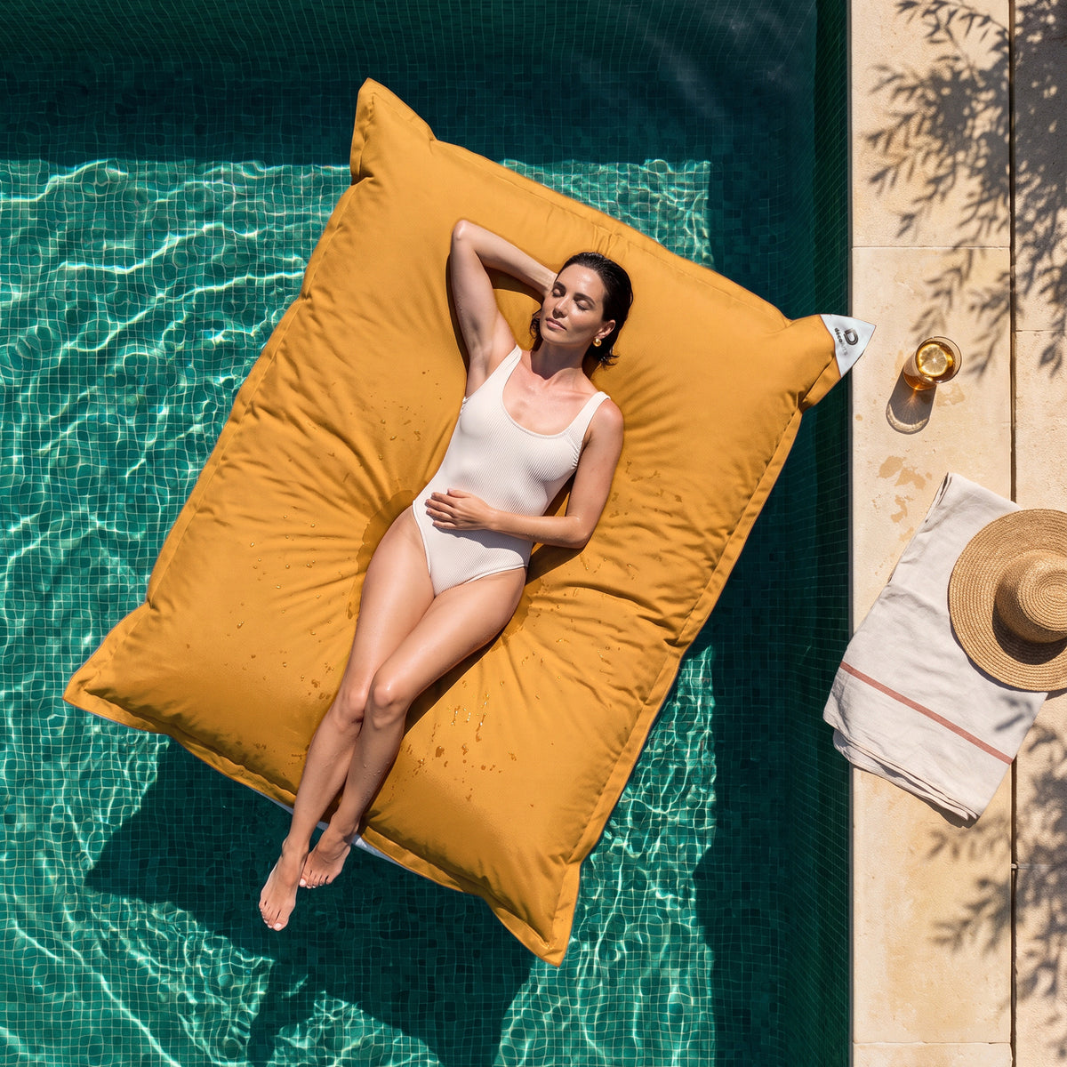 Puf gigante flotante 180 × 140 cm Amarillo Miel en una piscina, mujer tumbada al sol, vista cenital
