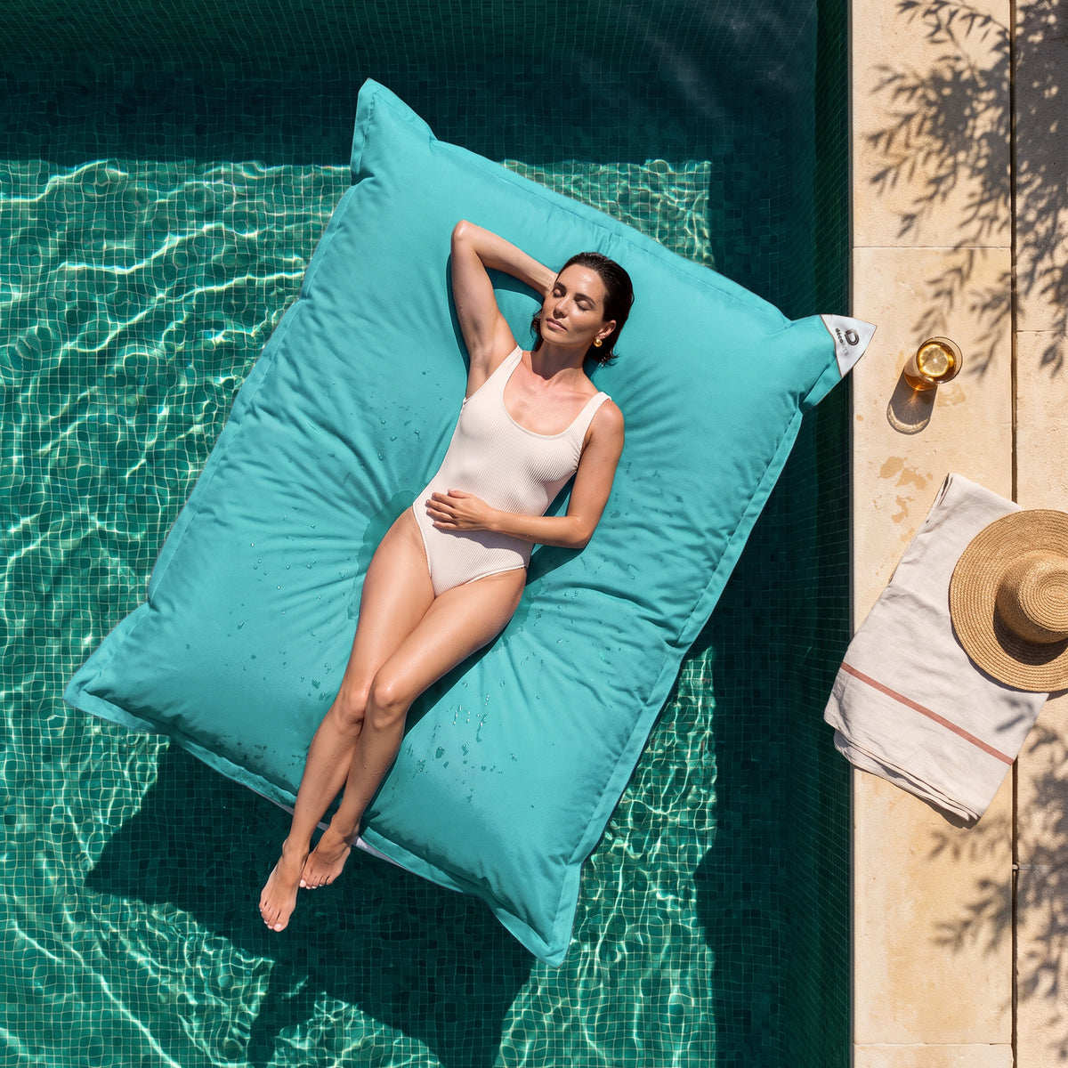 Solo funda, para rellenar – Puf gigante flotante 180 × 140 cm Azul Caribe en una piscina, mujer tumbada al sol, vista cenital